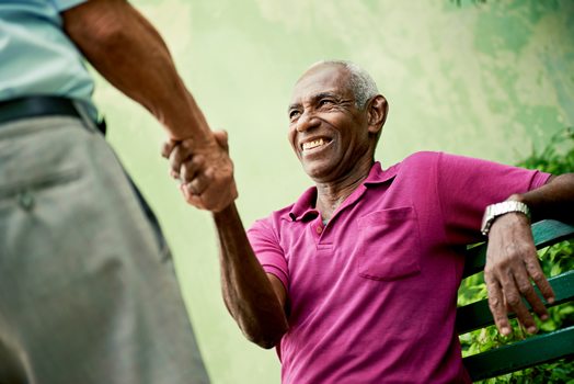 Two men shaking hands, one smiling on a park bench
