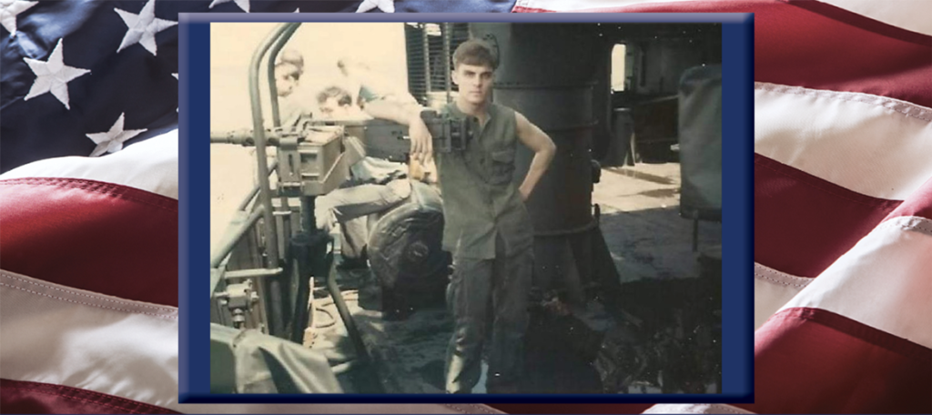 Walter Nichols, Veteran of the Month, as a young sailor standing by a mounted machine gun in the Mekong Delta, 1969