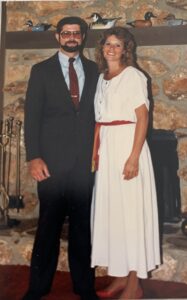 Frank Guerrettaz and Margo dressed up and smiling in front of a stone fireplace